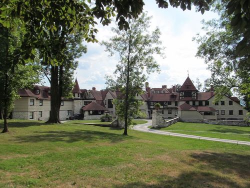 Historic building with a red-roofed structure, surrounded by trees and a grassy area under a blue sky.