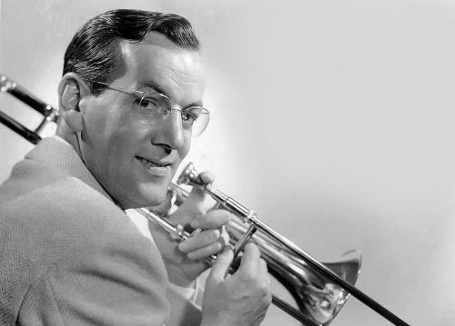 A smiling man in a suit holds a trombone, posing for a black-and-white photo.