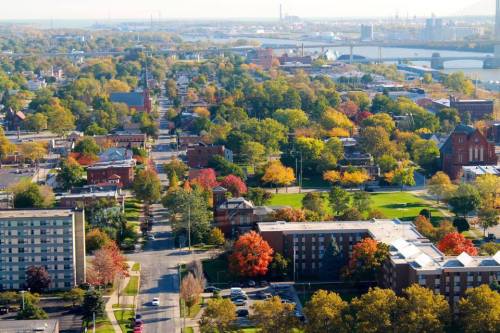Aerial view of a vibrant cityscape with colorful autumn trees, buildings, and a river in the background.