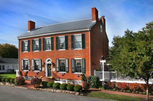 A two-story brick house with green shutters, a porch, and landscaped gardens under a clear blue sky.