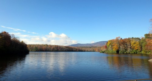A serene lake surrounded by colorful autumn trees under a clear blue sky and distant mountains.