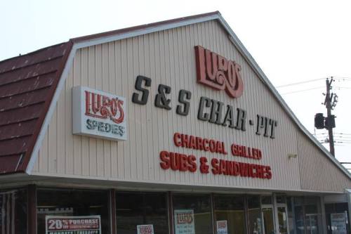 Exterior of a restaurant named "Lugo's S&S Char-Pit," featuring a sign for charcoal grilled subs and sandwiches.