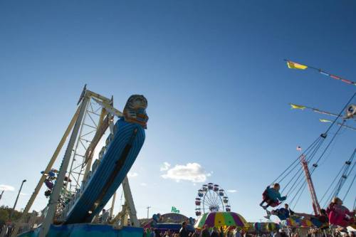 A vibrant carnival scene with rides, a ferris wheel, and clear blue skies.