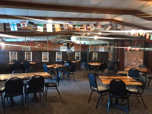 Interior of a spacious dining area with wooden tables, black chairs, and international flags hanging from the ceiling.