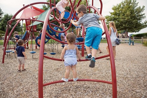 Children play on a colorful playground structure, climbing and exploring in a sunny outdoor setting.