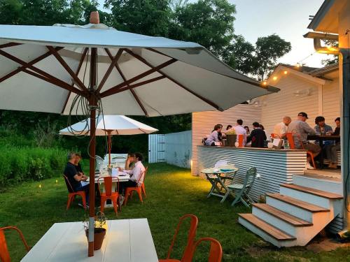 A cozy outdoor dining area with tables under umbrellas, people enjoying a meal, and greenery in the background.