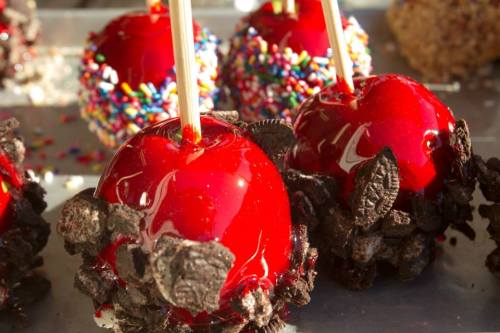 Close-up of red candy apples coated with crushed Oreos and colorful sprinkles on a silver tray.