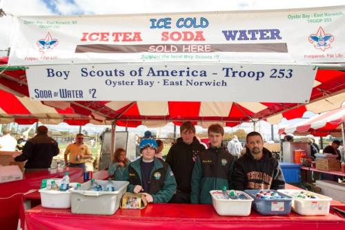 Boy Scouts Troop 253 selling ice tea, soda, and water at a booth, with four members behind the counter.