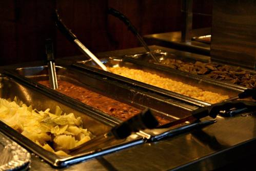 A buffet setup with metal trays containing various dishes, including beans, corn, and chopped cabbage.
