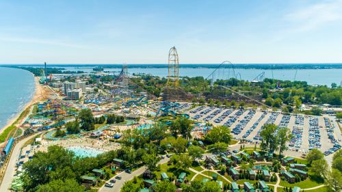 Aerial view of a theme park with roller coasters, a water park, and a large parking lot near a lake.