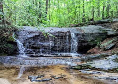 A serene waterfall cascading over rocks, surrounded by lush green trees in a tranquil forest setting.