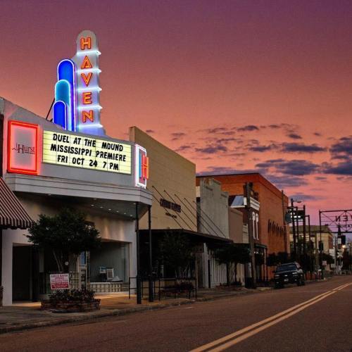 A vintage theater marquee announces the "Duel at the Mound" premiere, set against a colorful sunset sky.