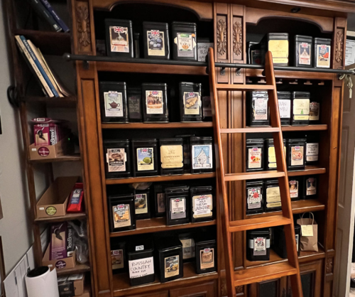A wooden shelf with labeled jars and a ladder, showcasing various spices and ingredients in a cozy kitchen setting.