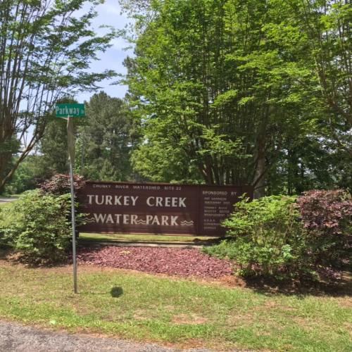 Sign for Turkey Creek Water Park surrounded by greenery and bushes, with a street sign for Parkway visible.