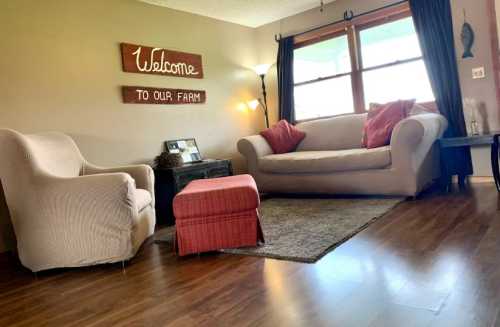 Cozy living room with a sofa, armchair, and a welcome sign, featuring warm lighting and a rustic decor.