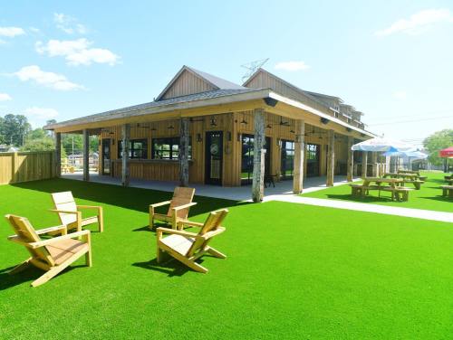 A rustic wooden building with outdoor seating on green turf, surrounded by trees and blue skies.