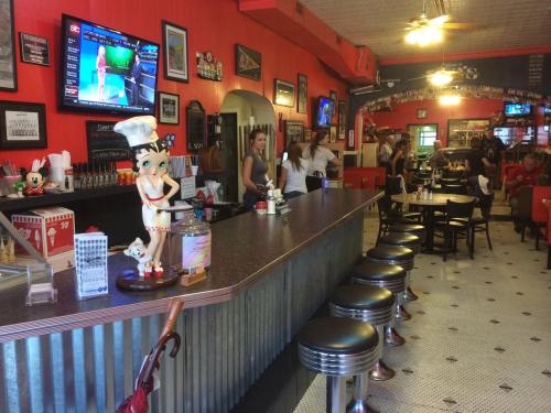 A retro diner interior with a long bar, vintage decor, and patrons enjoying food and drinks. TVs display sports.