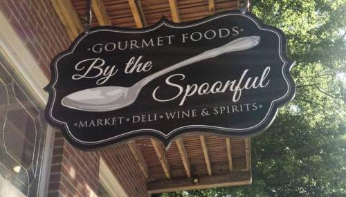 Sign for "By the Spoonful" featuring a spoon graphic, advertising gourmet foods, market, deli, wine, and spirits.
