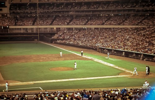 A crowded baseball stadium with players on the field and spectators in the stands, capturing a lively game atmosphere.