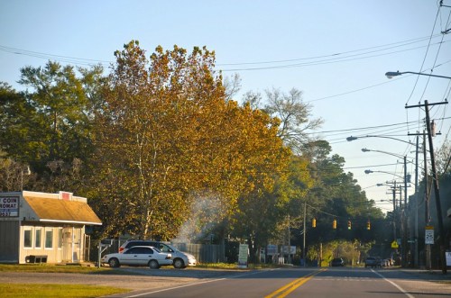 A quiet street scene with a car near a small building, surrounded by trees and power lines under a clear sky.