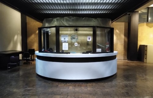 A modern reception desk with a circular shape, featuring a clock and safety equipment, in a spacious lobby area.
