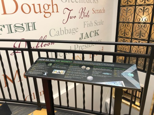 A display board with information about money, surrounded by colorful text on a wall.