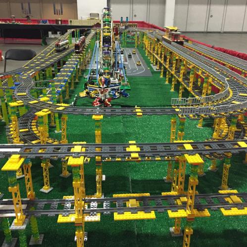 A colorful model train layout made of building blocks, featuring tracks, bridges, and a green base.