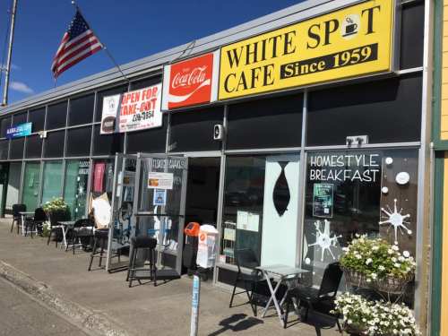 Exterior of White Spot Cafe, featuring outdoor seating, a sign for homestyle breakfast, and an American flag.