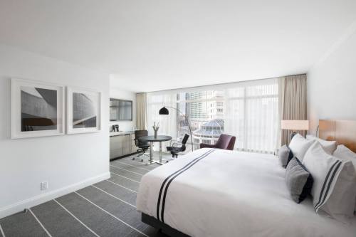 Modern hotel room featuring a king-sized bed, desk, and large windows with city views. Minimalist decor and natural light.