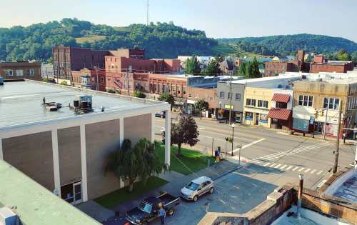 A view of a small town with buildings, trees, and hills in the background on a sunny day.