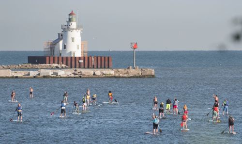 A group of people paddleboarding in the water near a lighthouse on a sunny day.