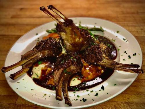 A plate of four lamb chops with a rich sauce, served with mashed potatoes and green beans, garnished with parsley.