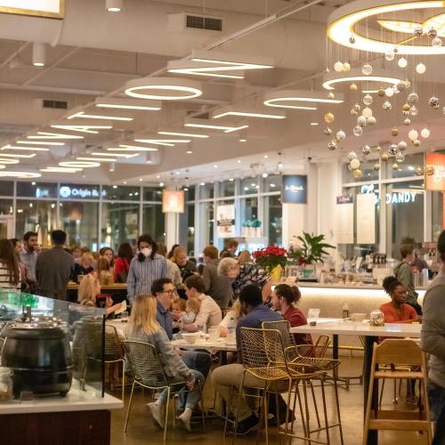A bustling café with people socializing, modern decor, and festive hanging ornaments.