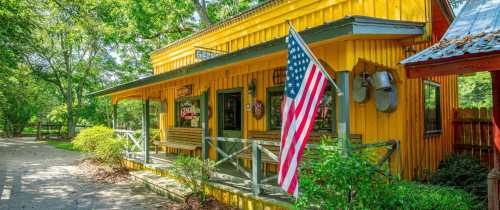 A bright yellow building with a porch, featuring an American flag and surrounded by greenery.