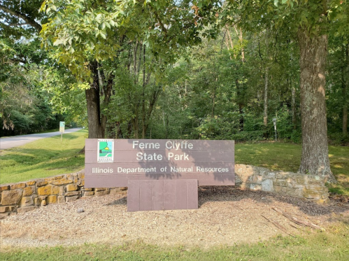 Sign for Ferne Clyffe State Park, surrounded by trees, with a road visible in the background.