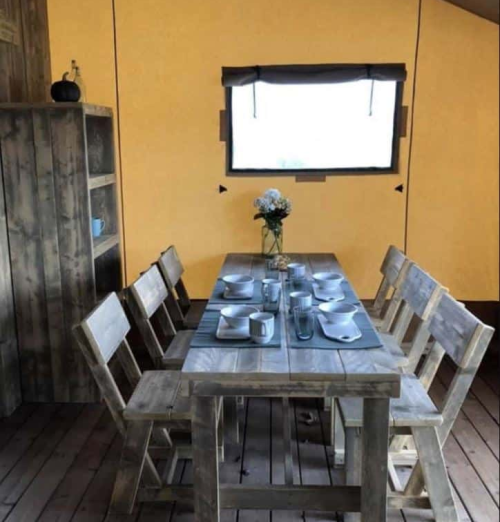 A rustic dining area with a wooden table set for eight, featuring plates, glasses, and a vase of flowers.