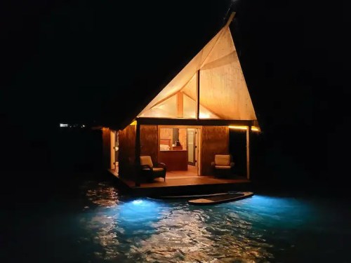 A cozy wooden cabin on water, illuminated at night, with soft lighting and a serene atmosphere.