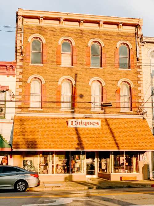 A vintage brick building with arched windows and a shopfront labeled "Uniques," featuring a car parked outside.