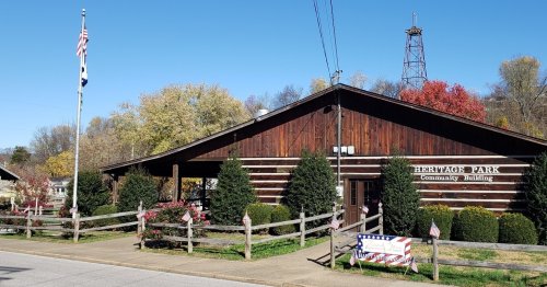 A wooden community building with a flagpole, surrounded by greenery and autumn trees, in Heritage Park.
