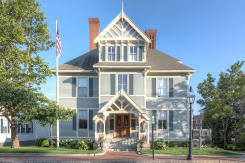 A large, light blue Victorian-style house with a front porch, flagpole, and well-maintained landscaping.