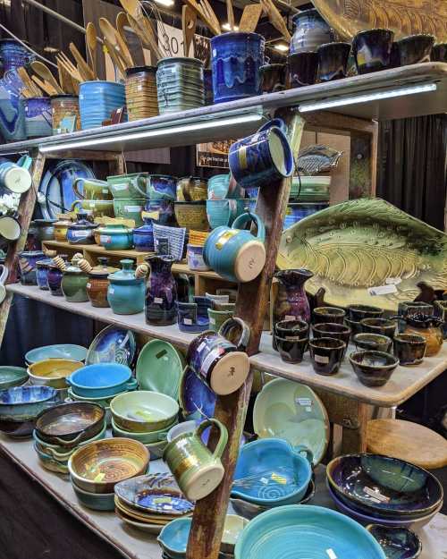 A display of colorful pottery, including bowls, mugs, and decorative pieces, arranged on wooden shelves.