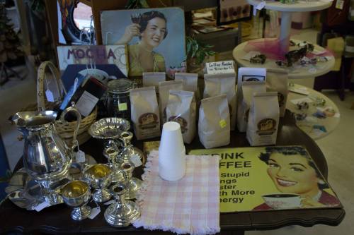 A vintage display featuring coffee bags, silverware, and a retro sign about coffee, set on a wooden table.