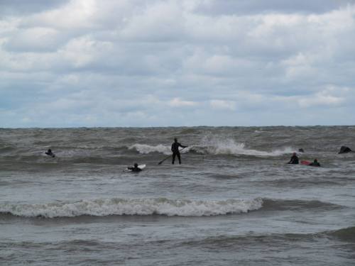 Surfers in wetsuits riding waves on a cloudy day at the beach.