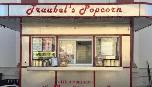 A vintage popcorn stand with a red and silver exterior, featuring a menu and jars of popcorn on display.
