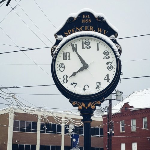 A vintage clock covered in snow, displaying the time in a snowy town square in Spencer, WV.