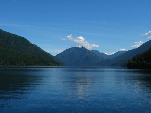 A serene lake surrounded by mountains under a clear blue sky with a few clouds.