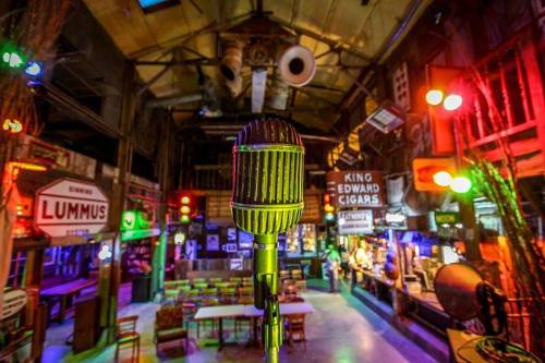 A vintage microphone in focus, with a colorful, lively bar setting and various signs in the background.
