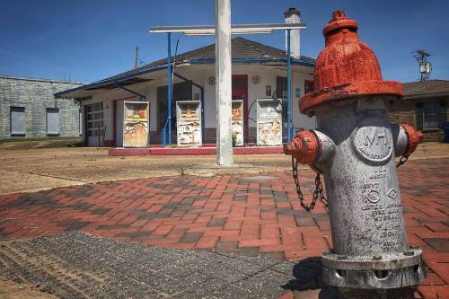 A weathered fire hydrant in the foreground, with an old building and blue sky in the background.