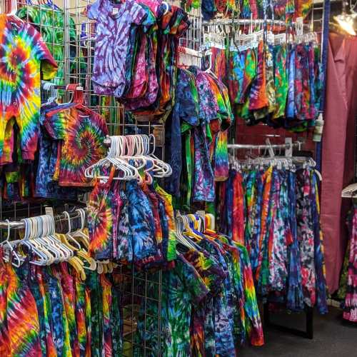 A vibrant display of tie-dye clothing in various colors, hanging on racks in a shop.
