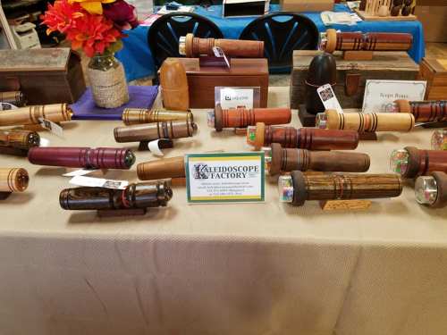 A display of various handcrafted wooden telescopes on a table, with a sign for "Telescope Factory" in the center.